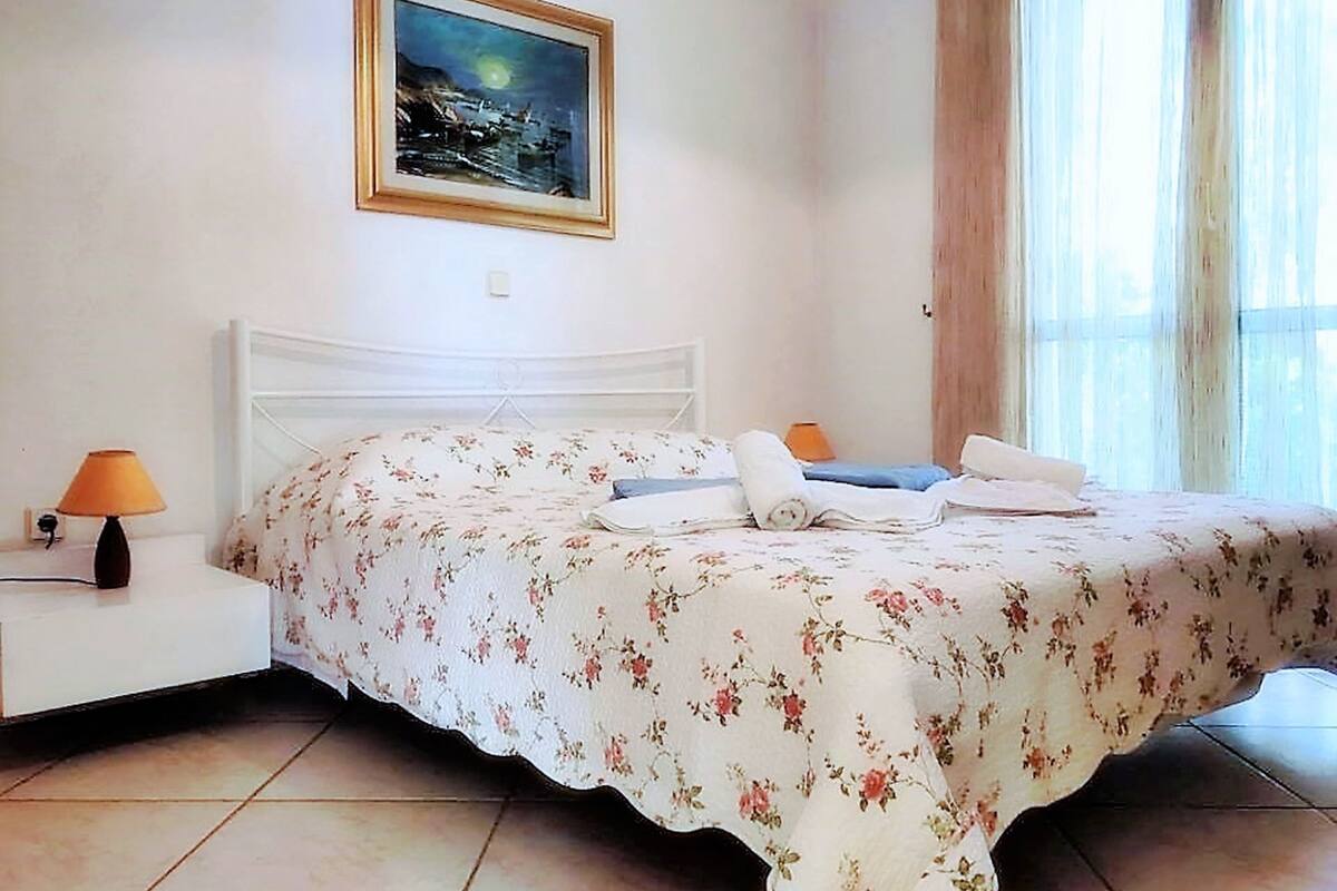 A bedroom with a bed, nightstand, lamp, and a painting on the wall.
