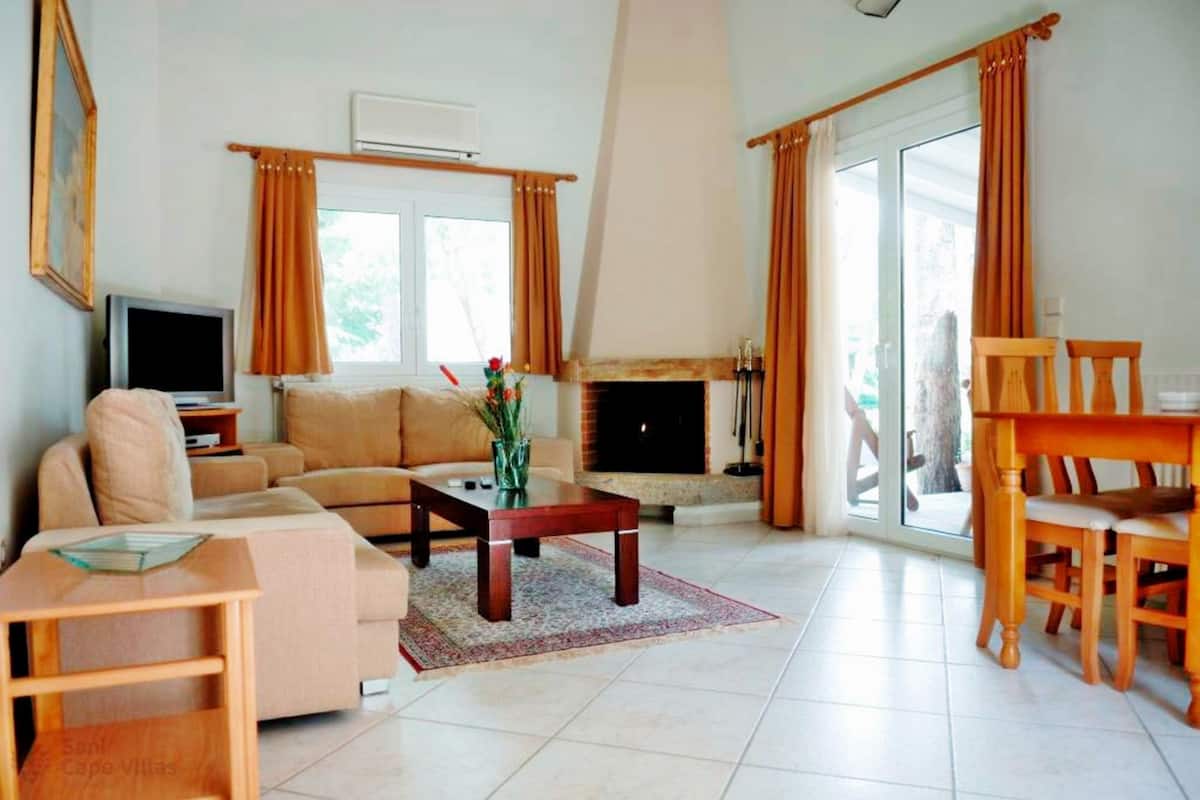 A spacious living room with a sofa, a coffee table, a fireplace, and a dining area with wooden chairs and a table.
