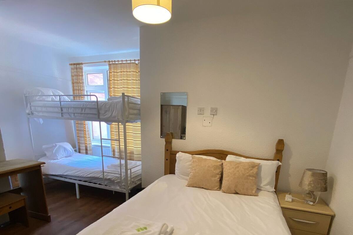 Ein Zimmer mit einem Etagenbett, einem Einzelbett mit Handtüchern, einem Schreibtisch und einem Nachttisch mit Lampe.