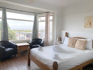 Una habitación de hotel con una cama, dos sillas, una mesita y un ventanal con cortinas.