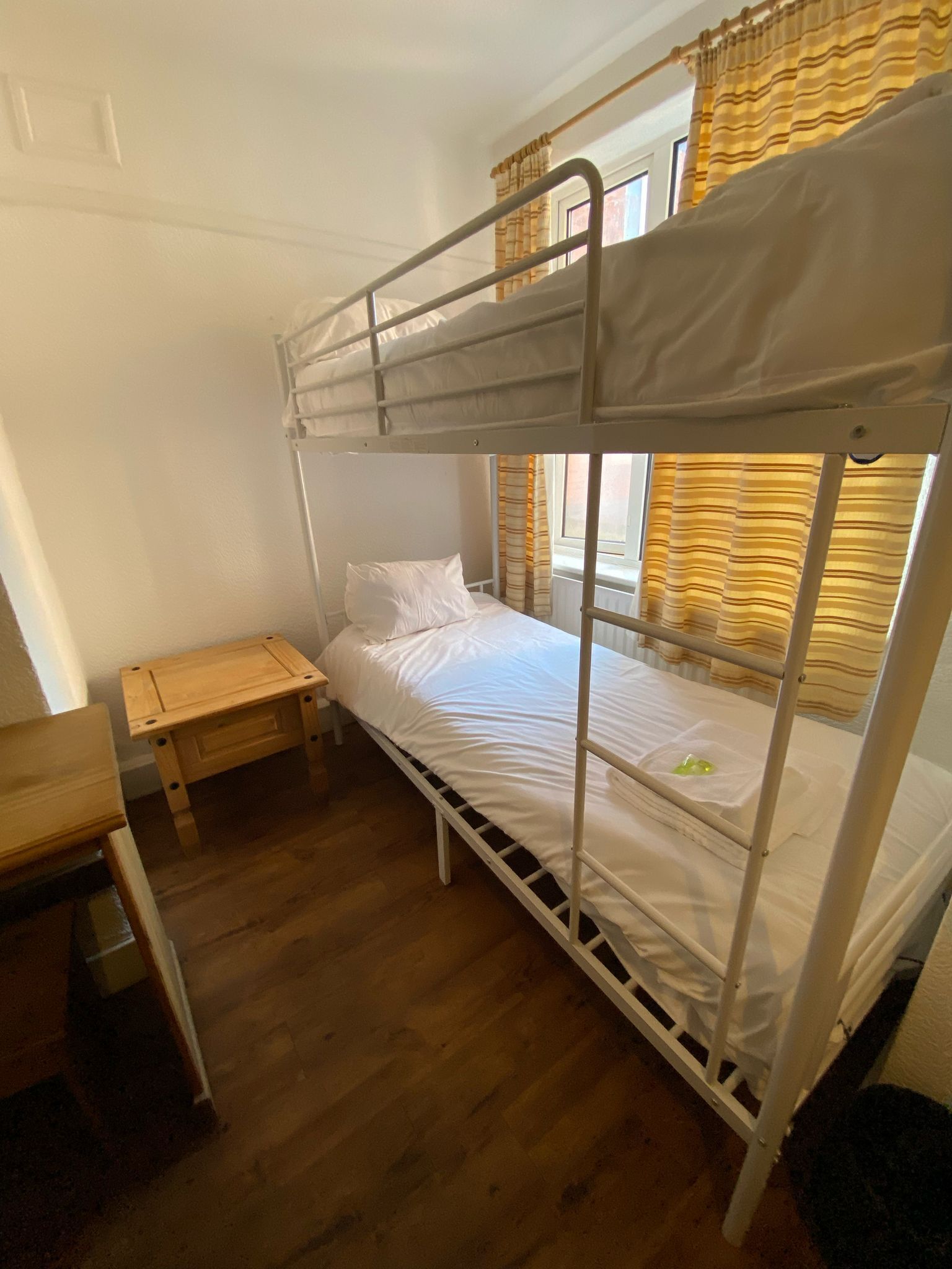 A bunk bed room with a wooden bench and a window with curtains.