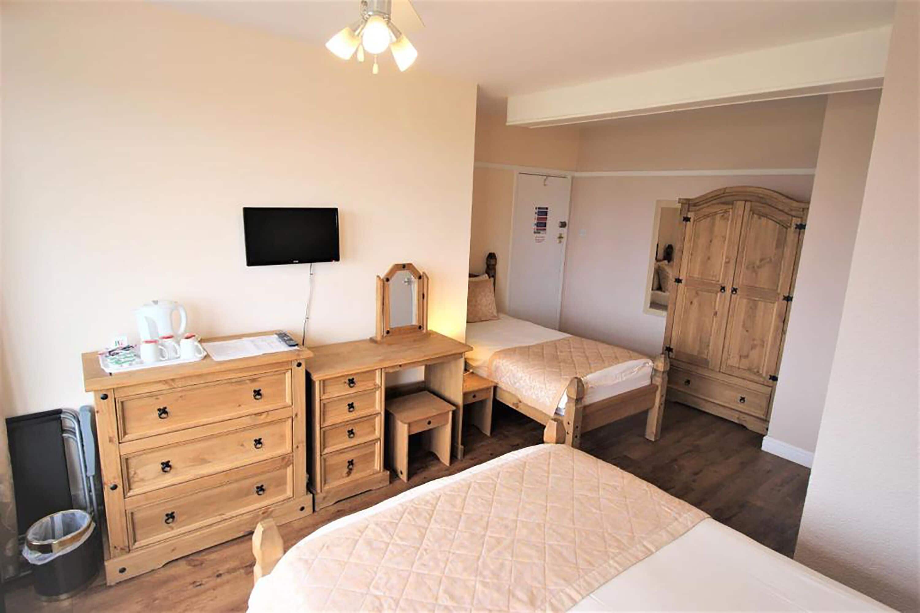 A bedroom with a bed, wooden dresser, TV, and wardrobe.