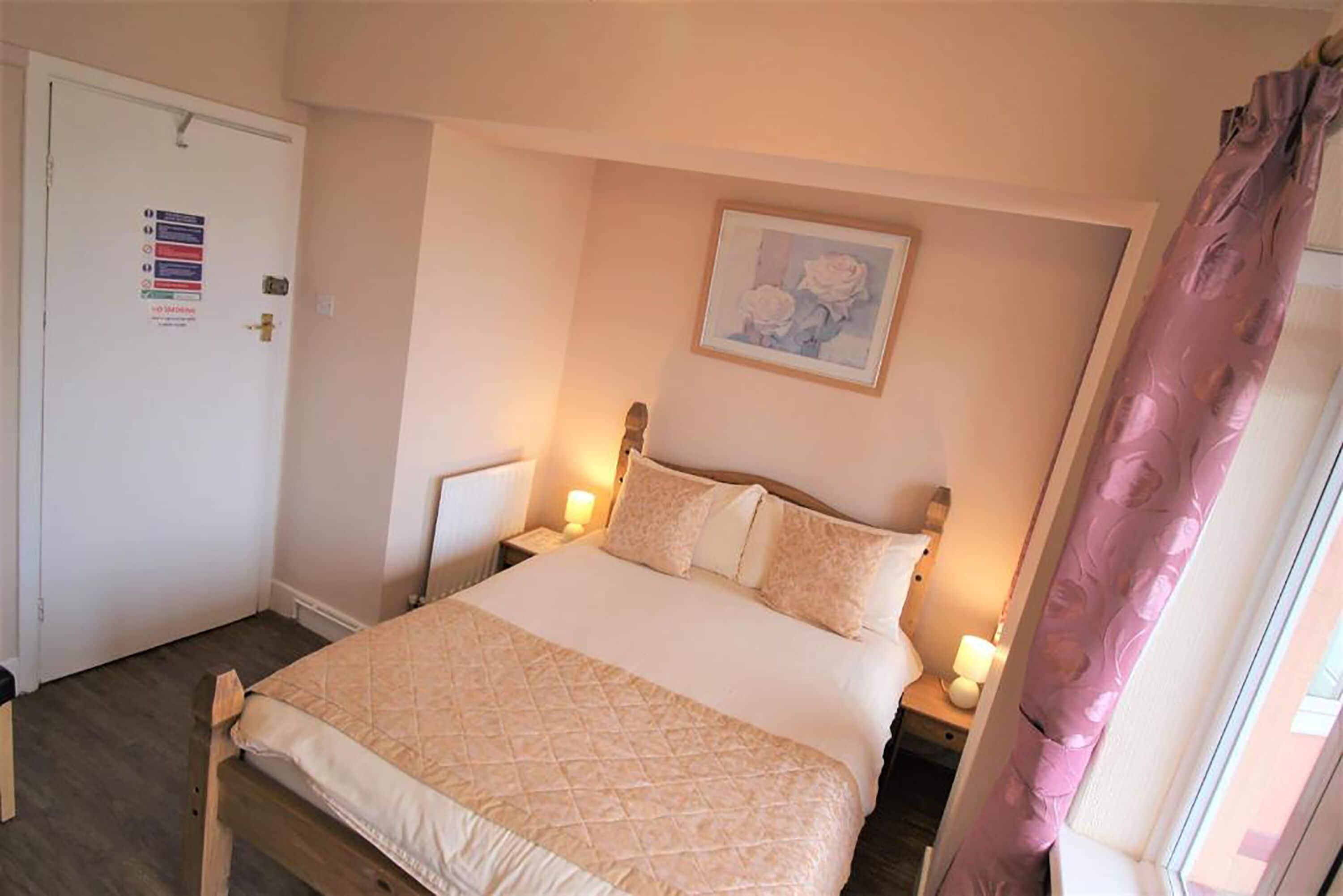 Une chambre à coucher avec un lit, des tables de chevet, une porte avec une pancarte, un tableau encadré au mur et une fenêtre avec des rideaux.