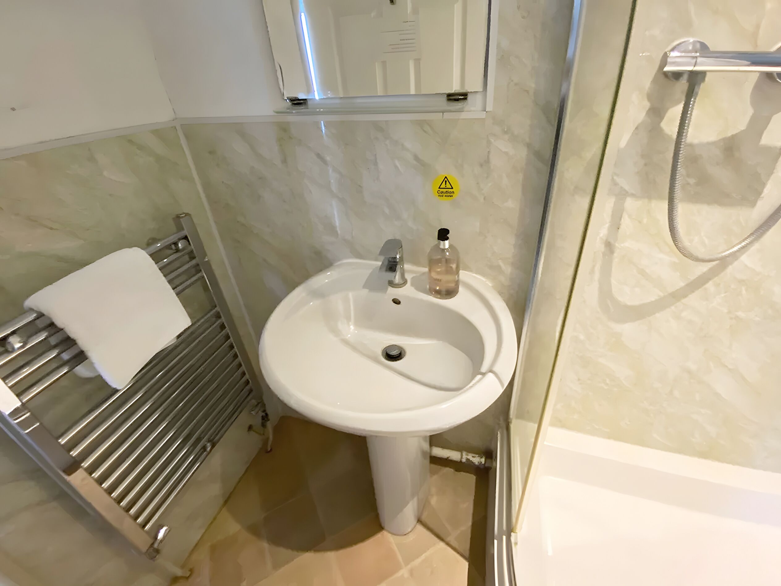 Un baño con lavamanos blanco, toallero y ducha.