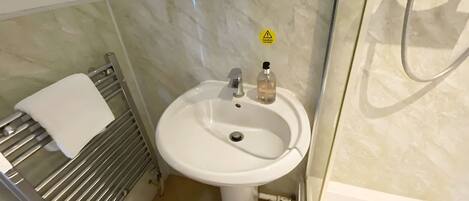 Un baño con lavamanos blanco, toallero y ducha.