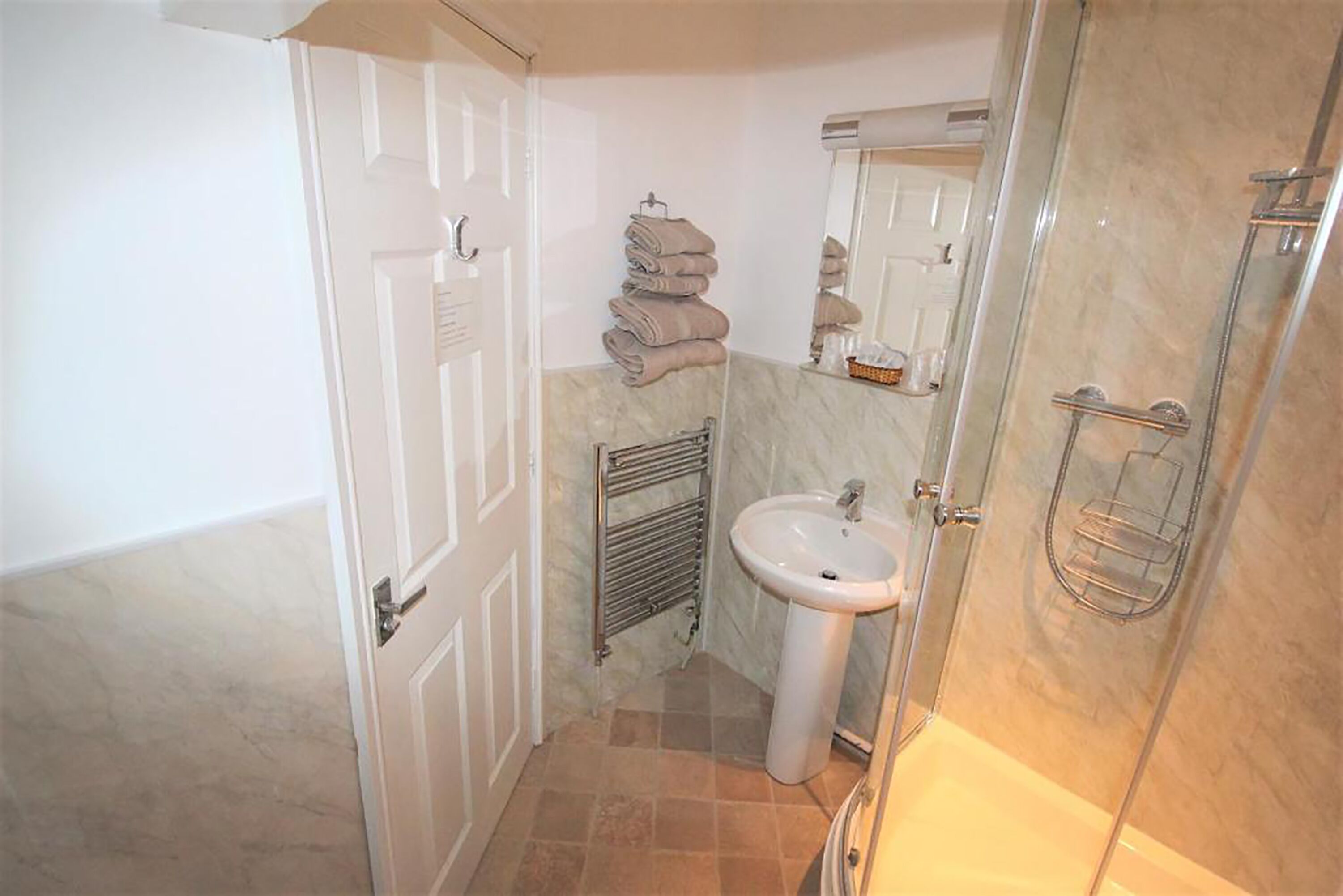 Un baño con una puerta blanca, un lavamanos, un perchero para toallas y una cabina de ducha con paredes de vidrio.
