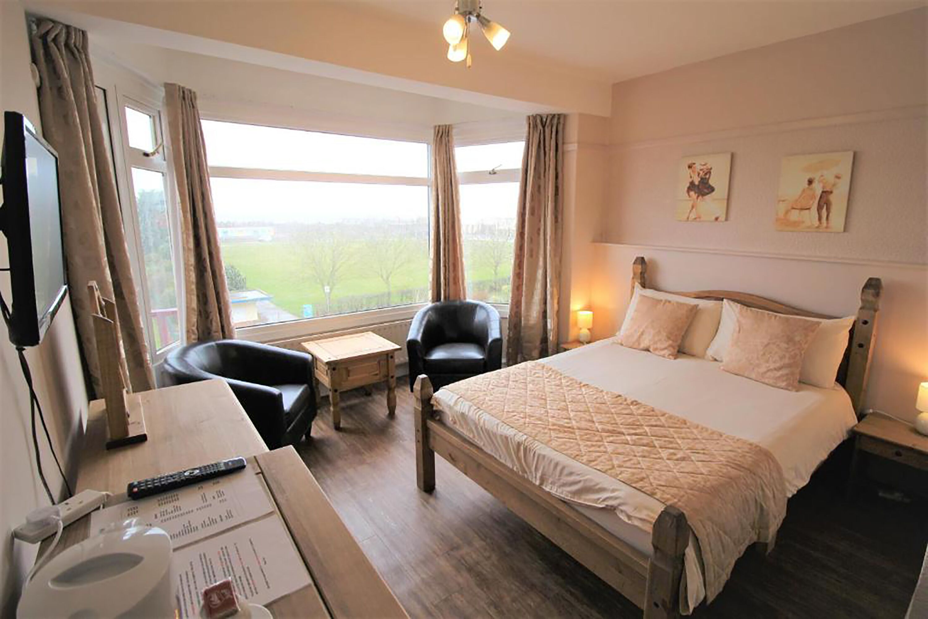 A hotel room with a large bed, a desk with a chair, a television, and a window with curtains.