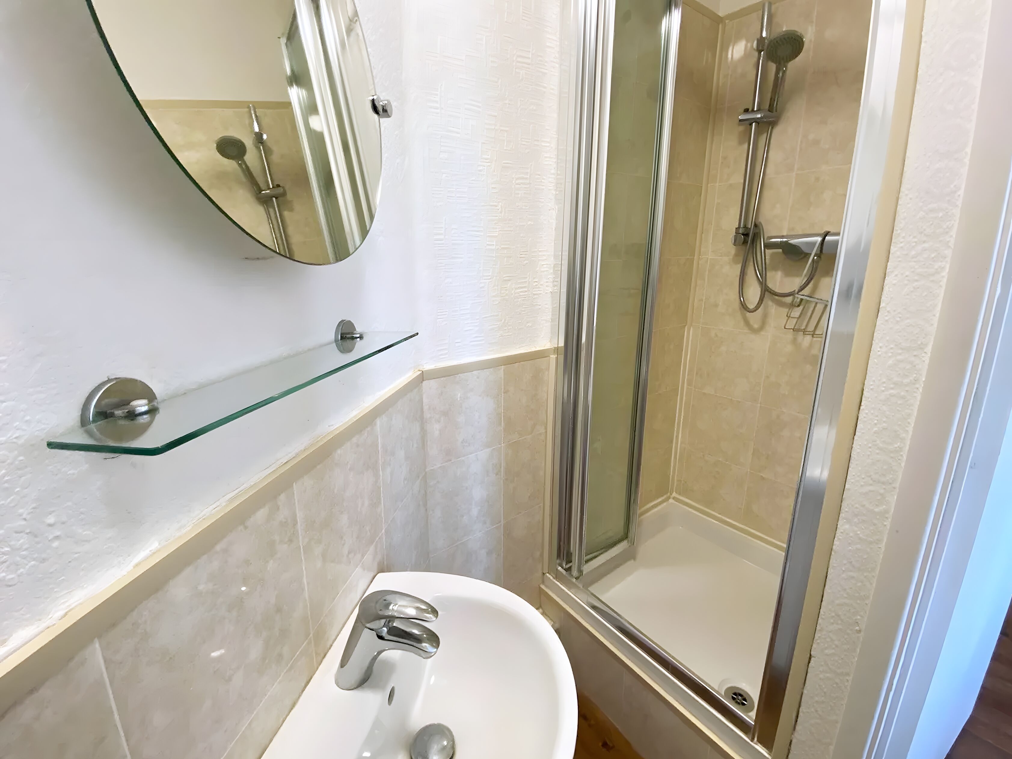 A bathroom with a glass shower enclosure, a white sink, and a glass shelf.
