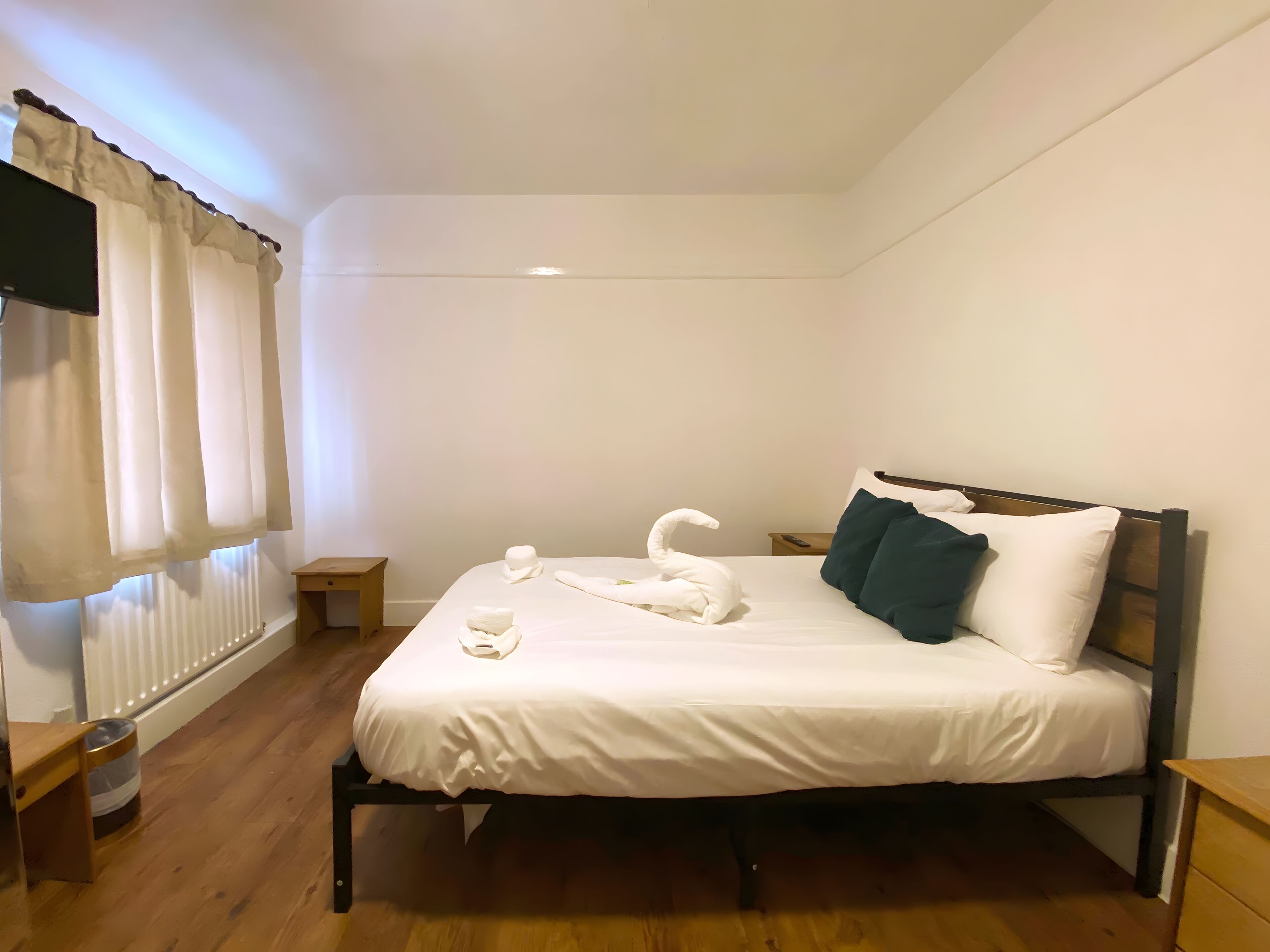 A neatly made bed with white linens and two decorative swan-shaped towels.