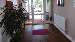 L’entrée d’un hôtel avec un plancher en bois, un tapis rouge, un radiateur et une grande plante.