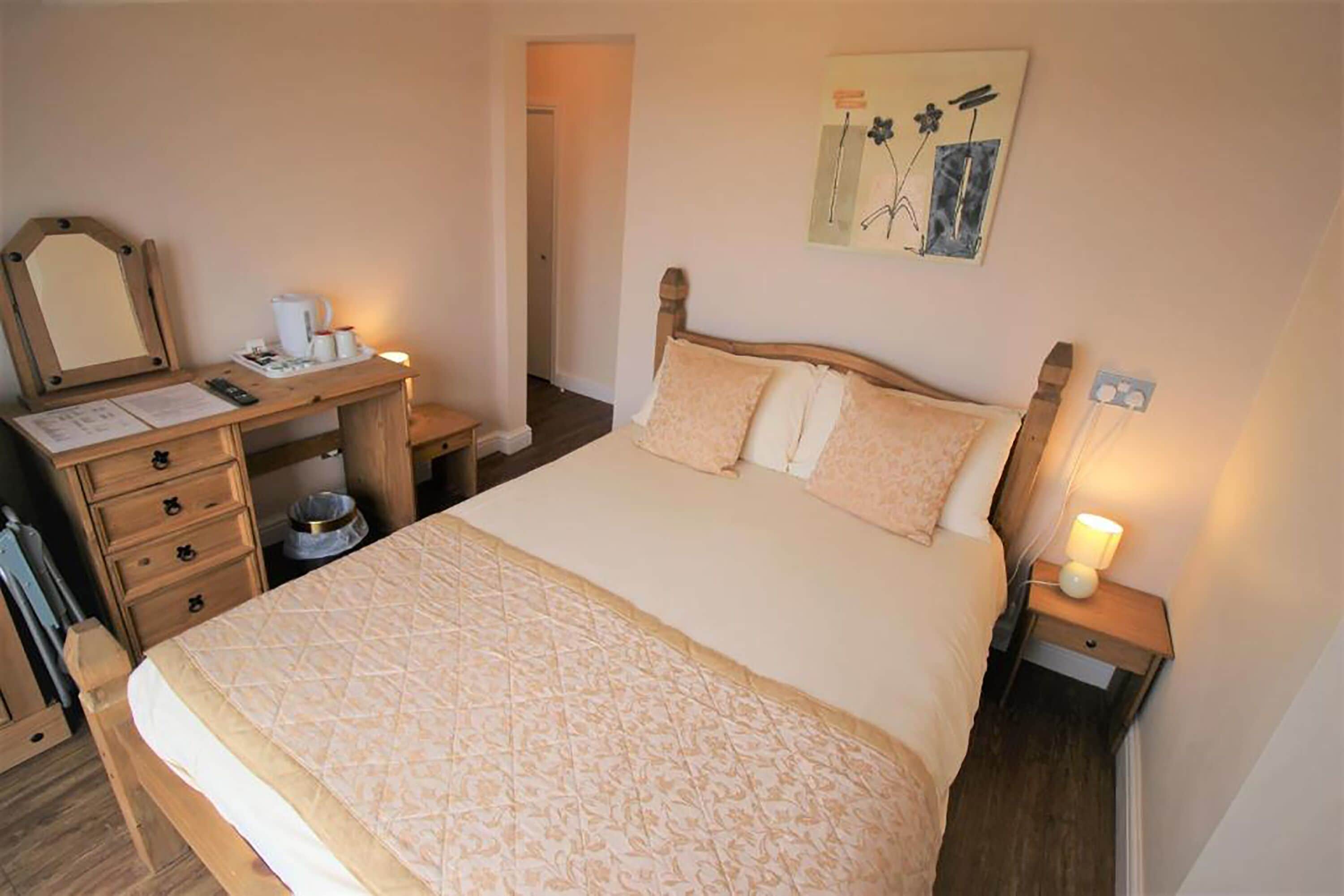 Une chambre à coucher comprenant un lit, des tables de chevet, un bureau, une chaise, un miroir et une porte.