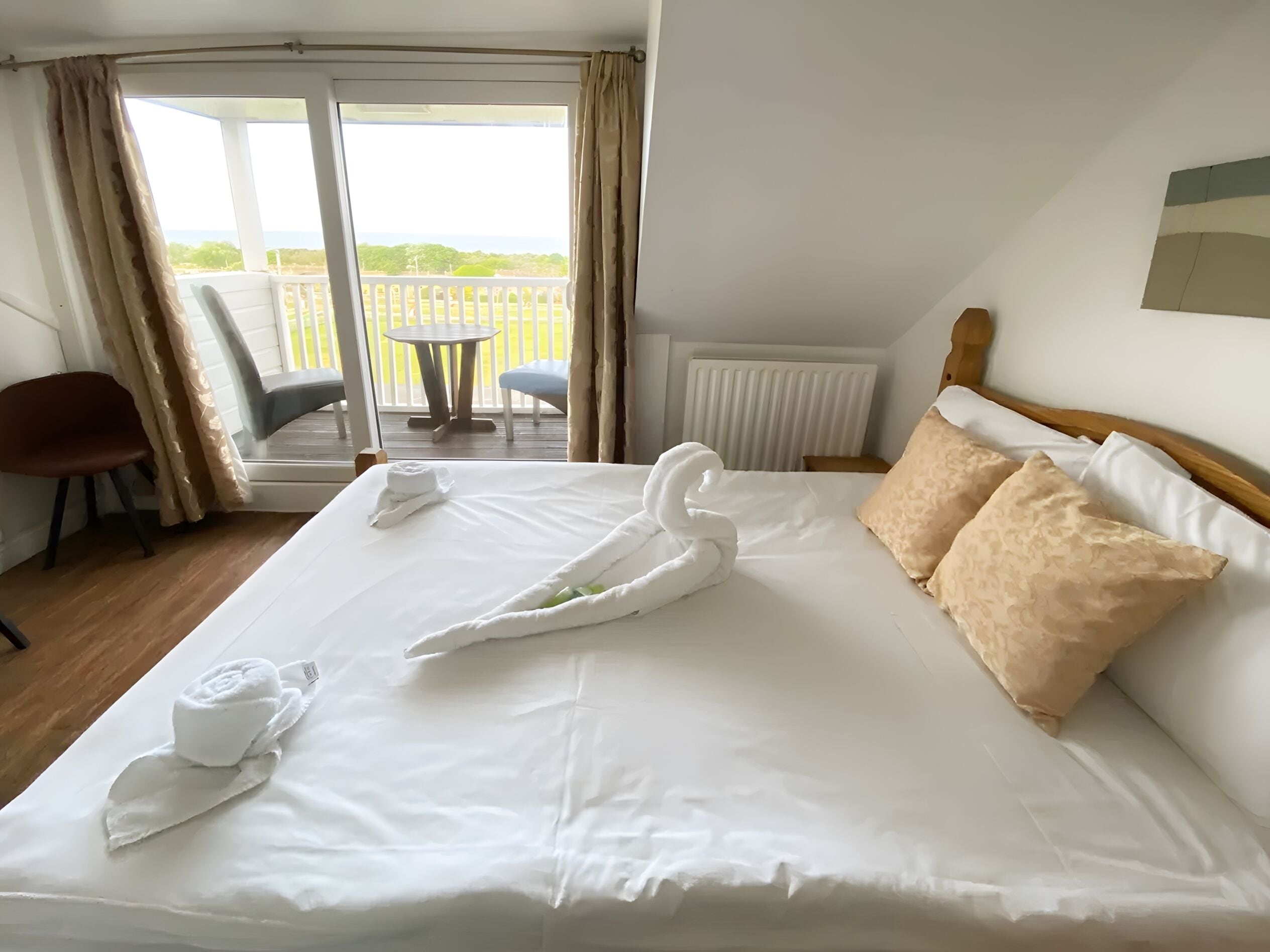 A hotel room with a large bed, a view of the outdoors, a chair, and a table.