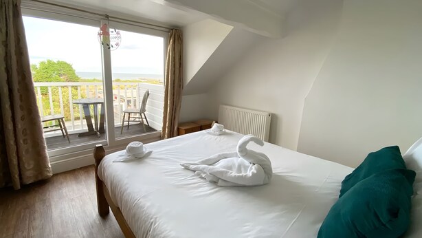 Une chambre d’hôtel avec un grand lit, un balcon avec une table et des chaises, et une vue sur la mer.