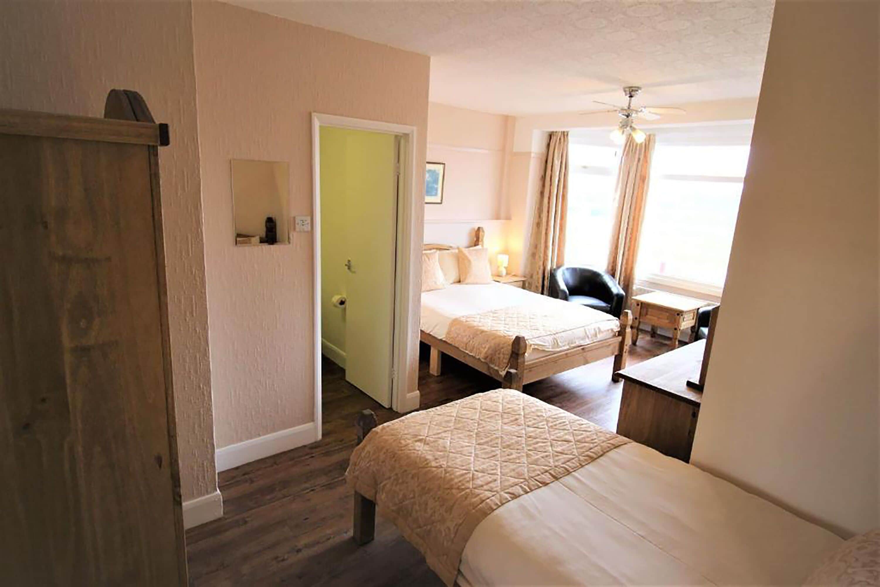 A hotel room with two beds, a desk, a chair, a ceiling fan, and a window with curtains.