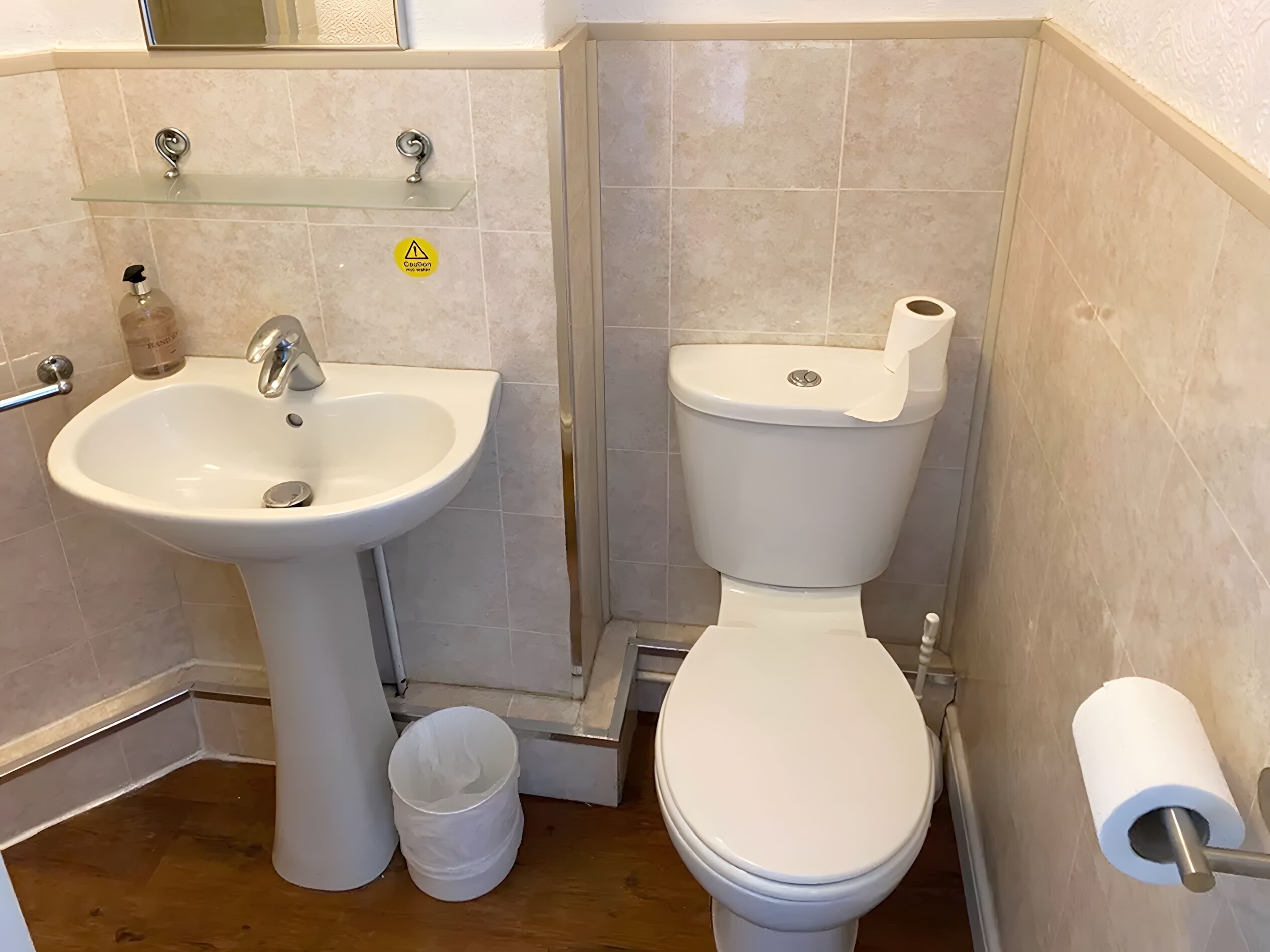 A bathroom with a white sink, toilet, and a trash bin.