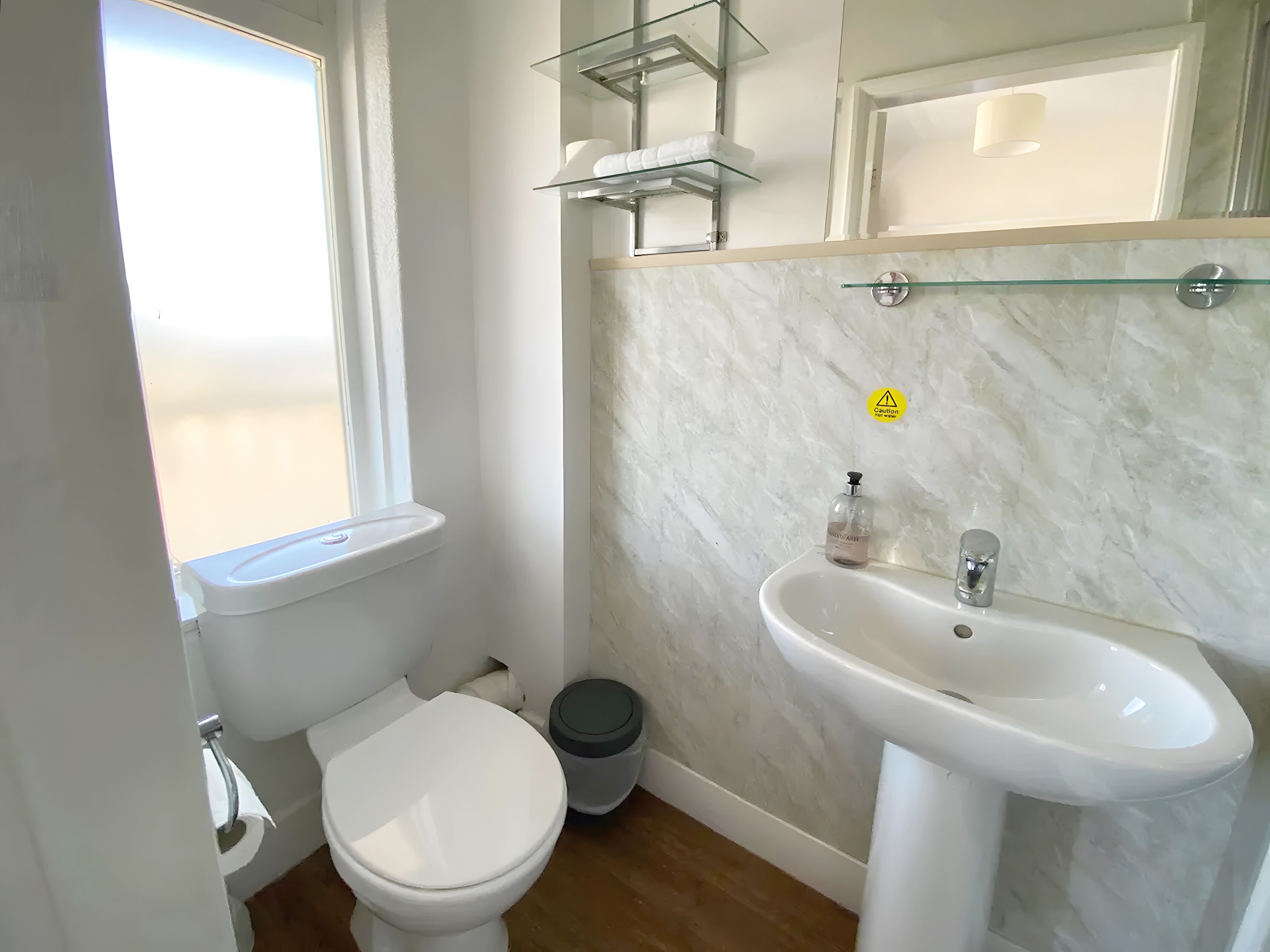 Une salle de bain équipée de toilettes, d’un lavabo et d’étagères en verre au-dessus du lavabo.