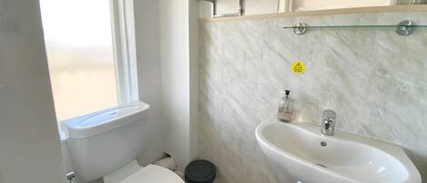 Une salle de bain équipée de toilettes, d’un lavabo et d’étagères en verre au-dessus du lavabo.