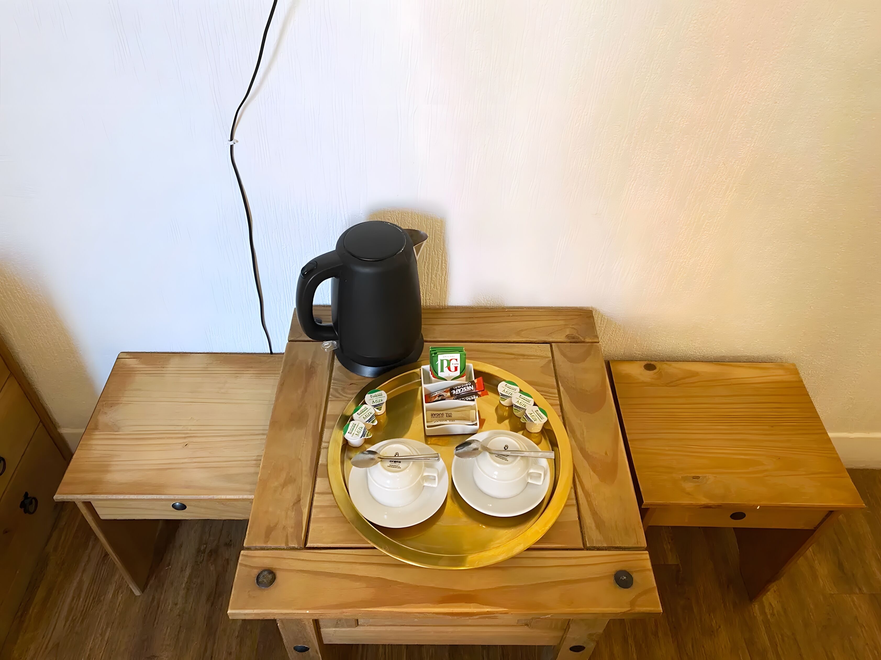 A wooden table with a tray holding a black kettle, two white cups, and several small containers, likely for condiments or spreads.