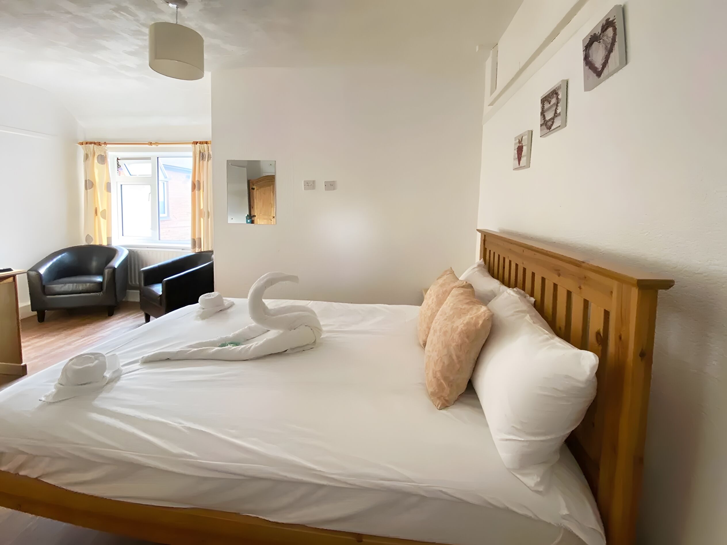 Een net opgemaakt bed met een houten hoofdbord, een handdoek in de vorm van een zwaan en twee kussens.