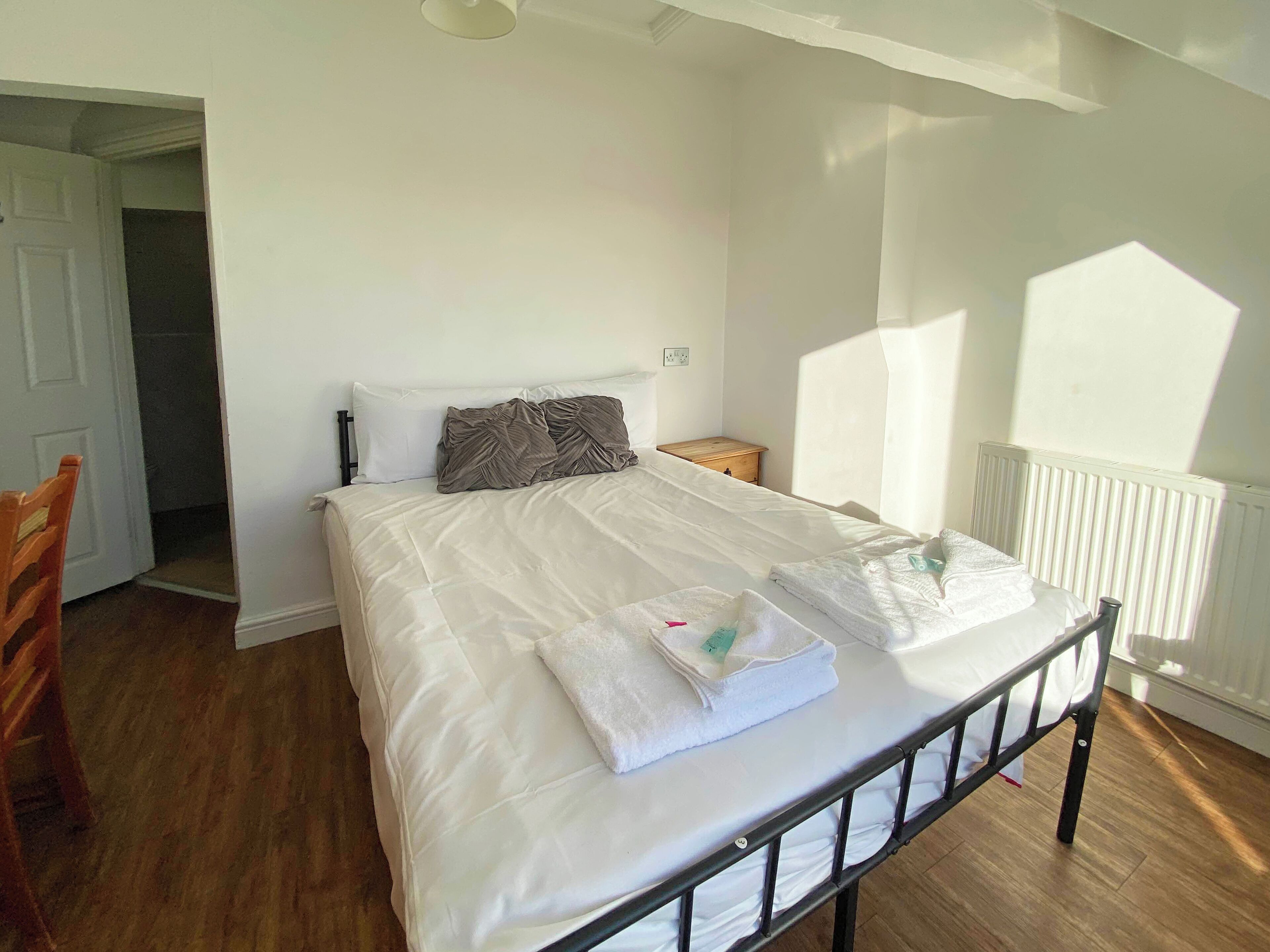A neatly made bed with white linens and towels, a wooden nightstand, and a white radiator.