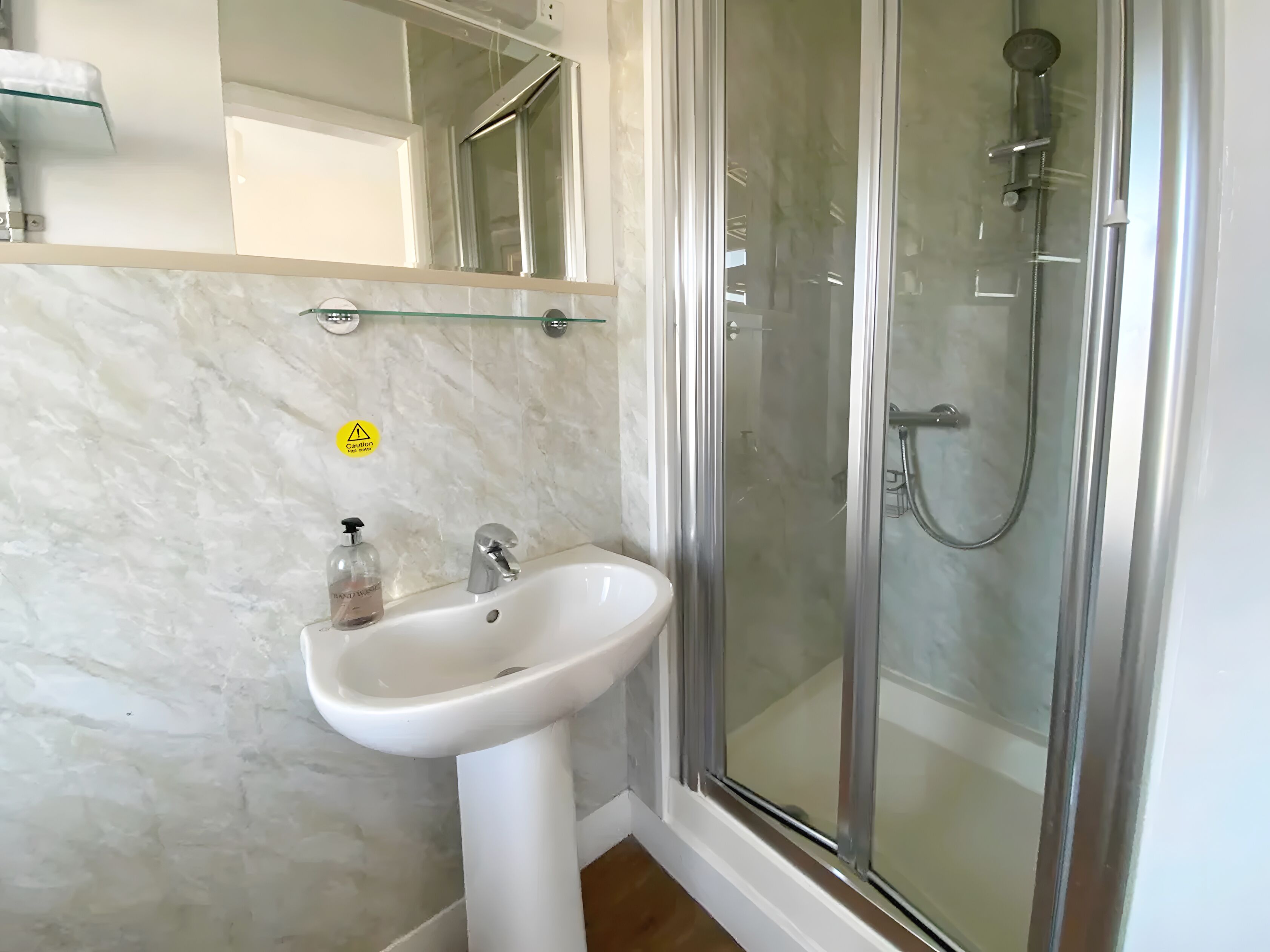 A bathroom with a white sink, a glass shower enclosure, and a caution sign on the wall.