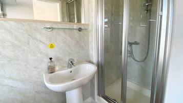 A bathroom with a white sink, a glass shower enclosure, and a caution sign on the wall.