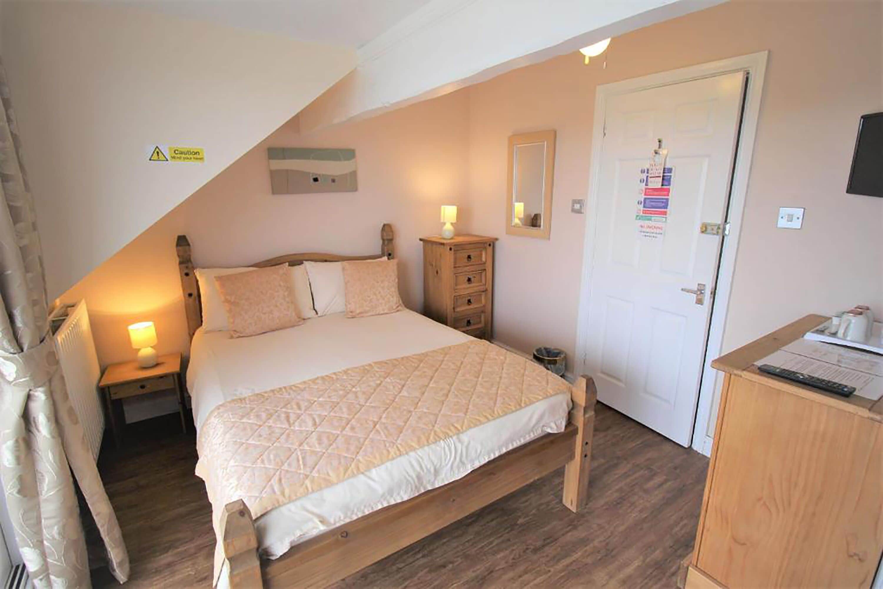 Un dormitorio con una cama, mesitas de noche, un aparador de madera, una puerta con un letrero y un pequeño armario.