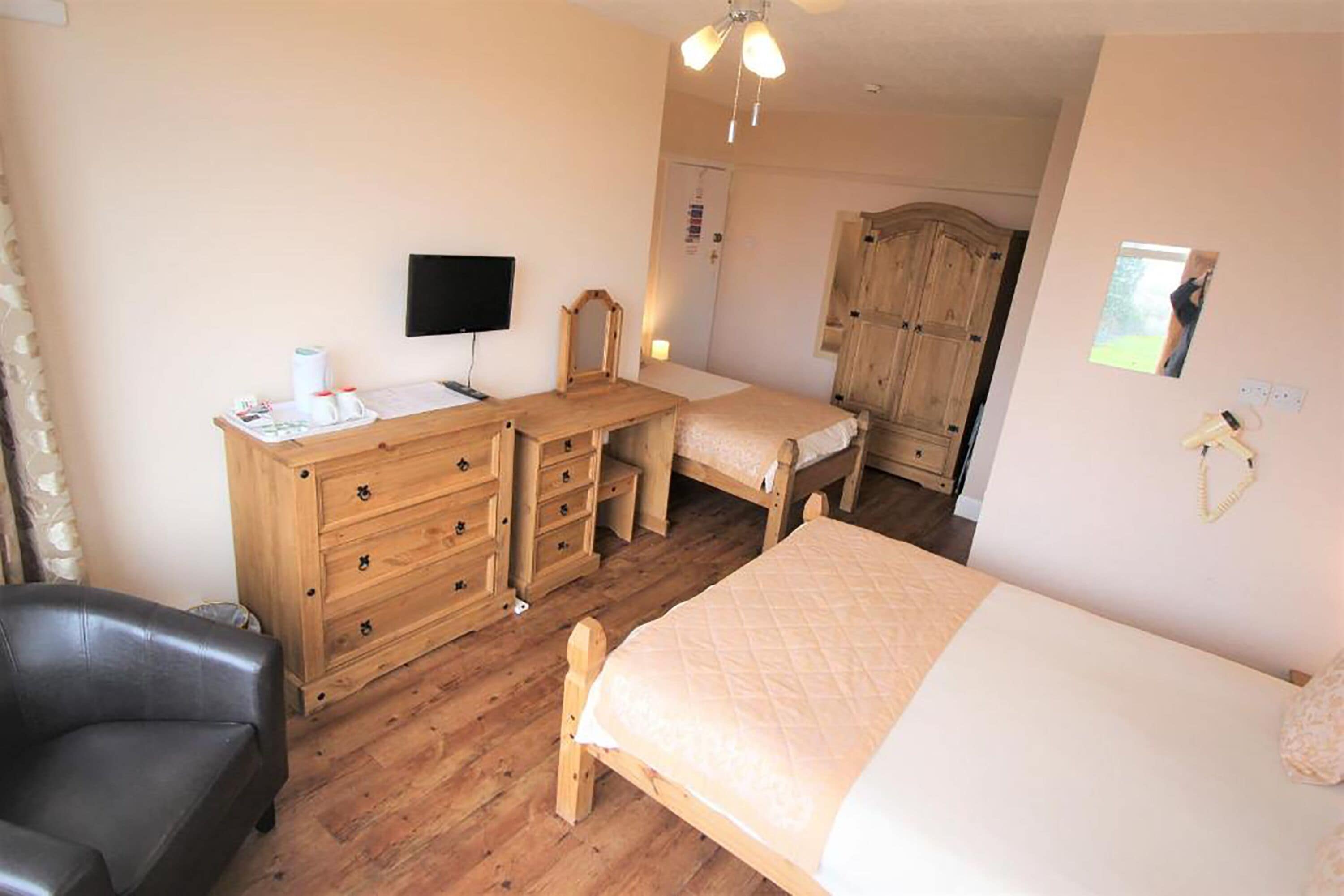 A bedroom with a wooden dresser, a desk, a bed, a chair, and a wardrobe.