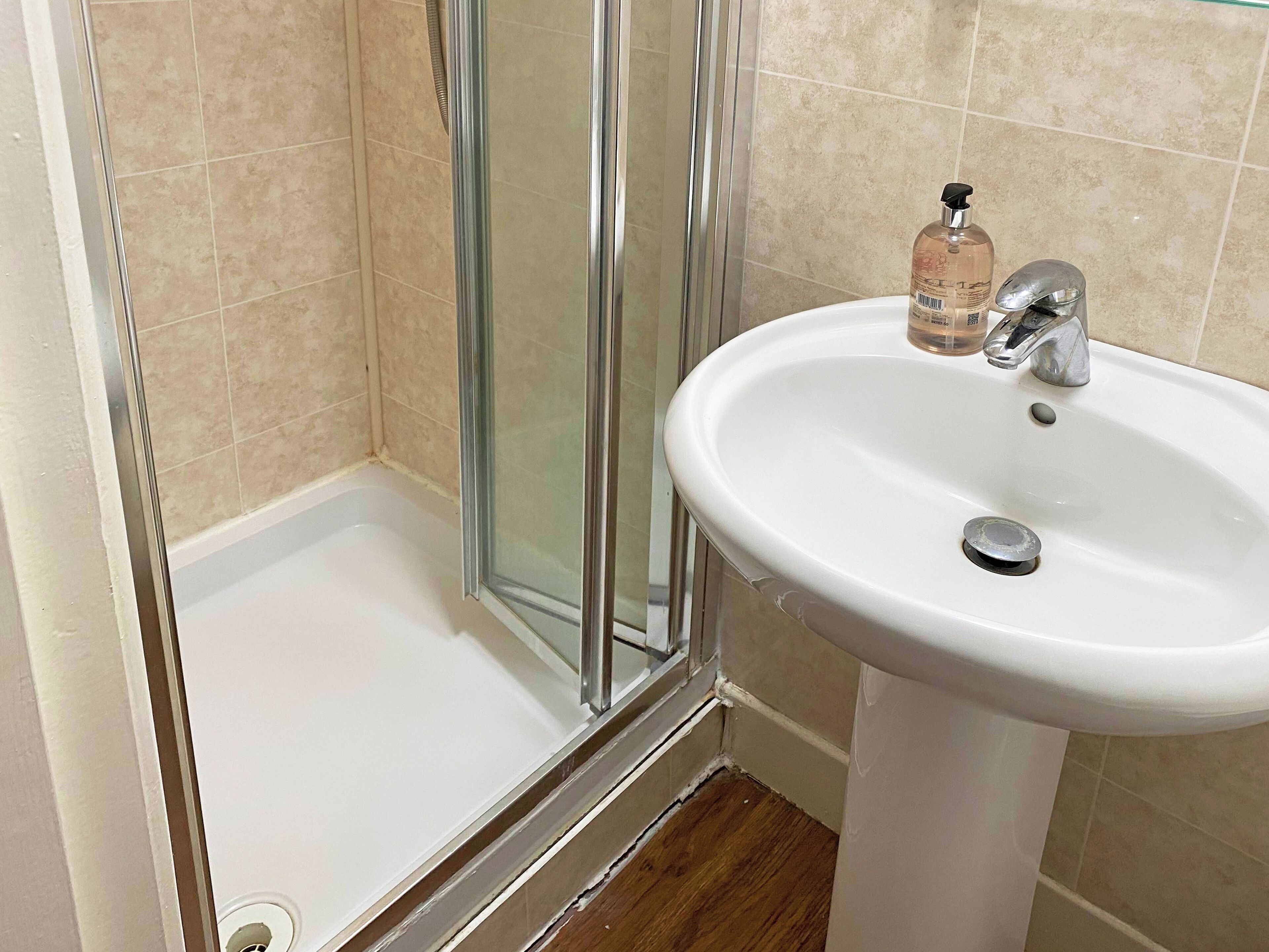 A bathroom with a white sink, a glass shower enclosure, and beige tiled walls.