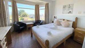 Une chambre d’hôtel avec un lit en bois, deux chaises, un bureau et une vue sur l’extérieur.