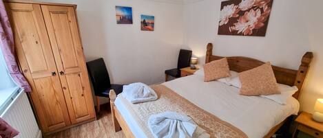 Un dormitorio ordenado con un armario de madera, una cama con ropa de cama estampada, una silla y dos cuadros colgados en la pared.
