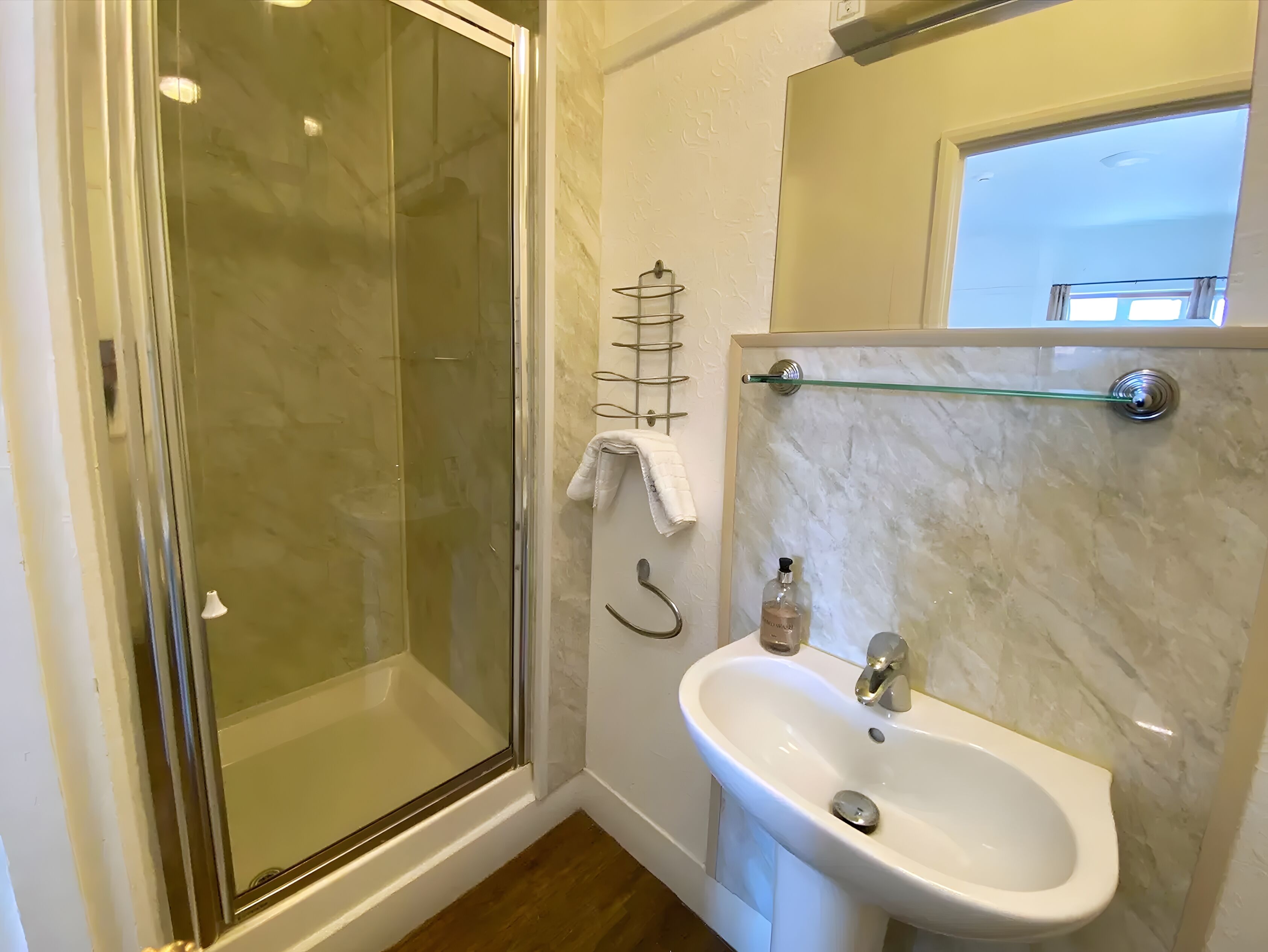 A modern bathroom with a glass-enclosed shower, a white sink, and a marble backsplash.