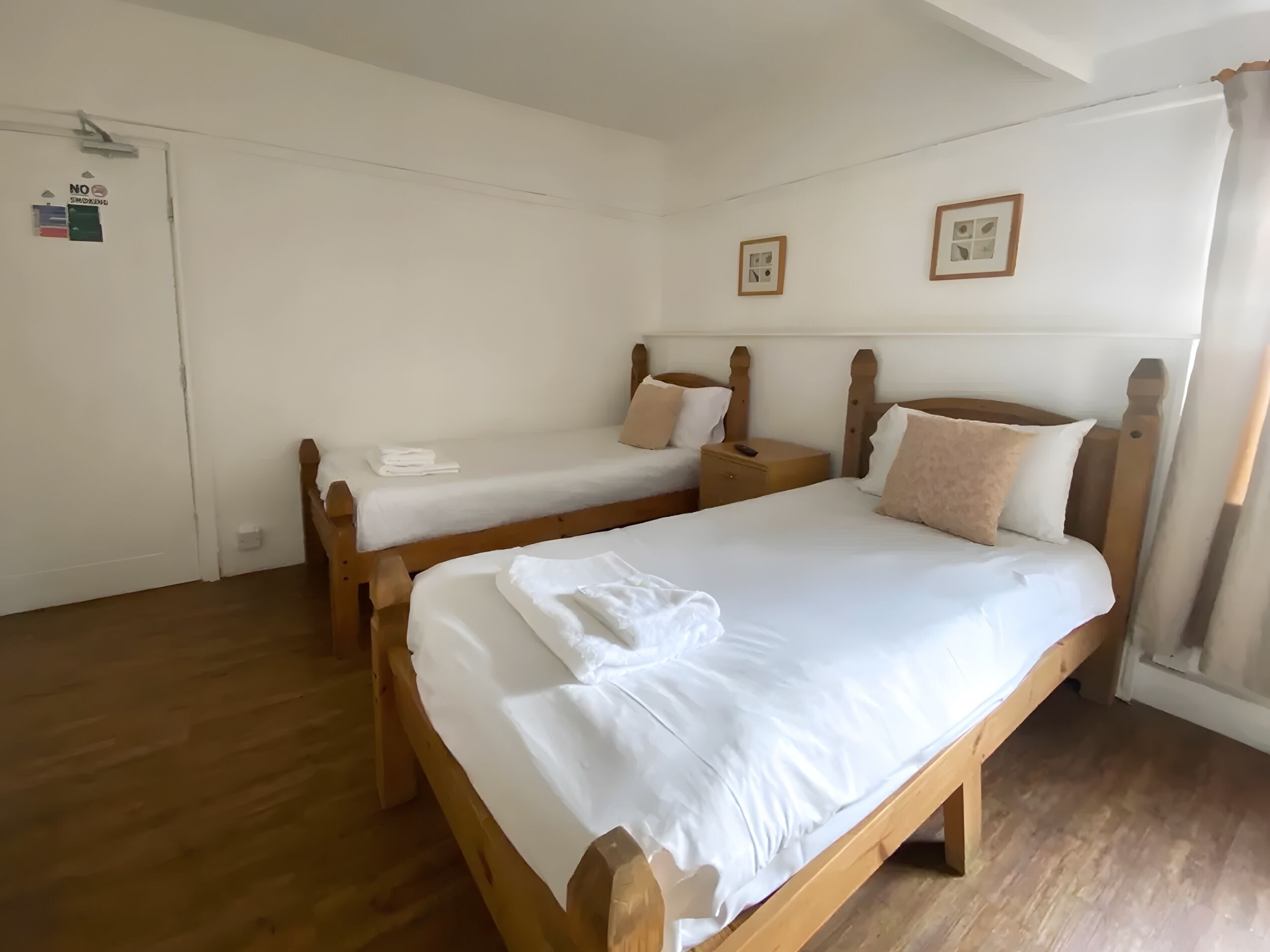 Una habitación con dos camas de madera, piso de madera y una puerta blanca con un cartel.