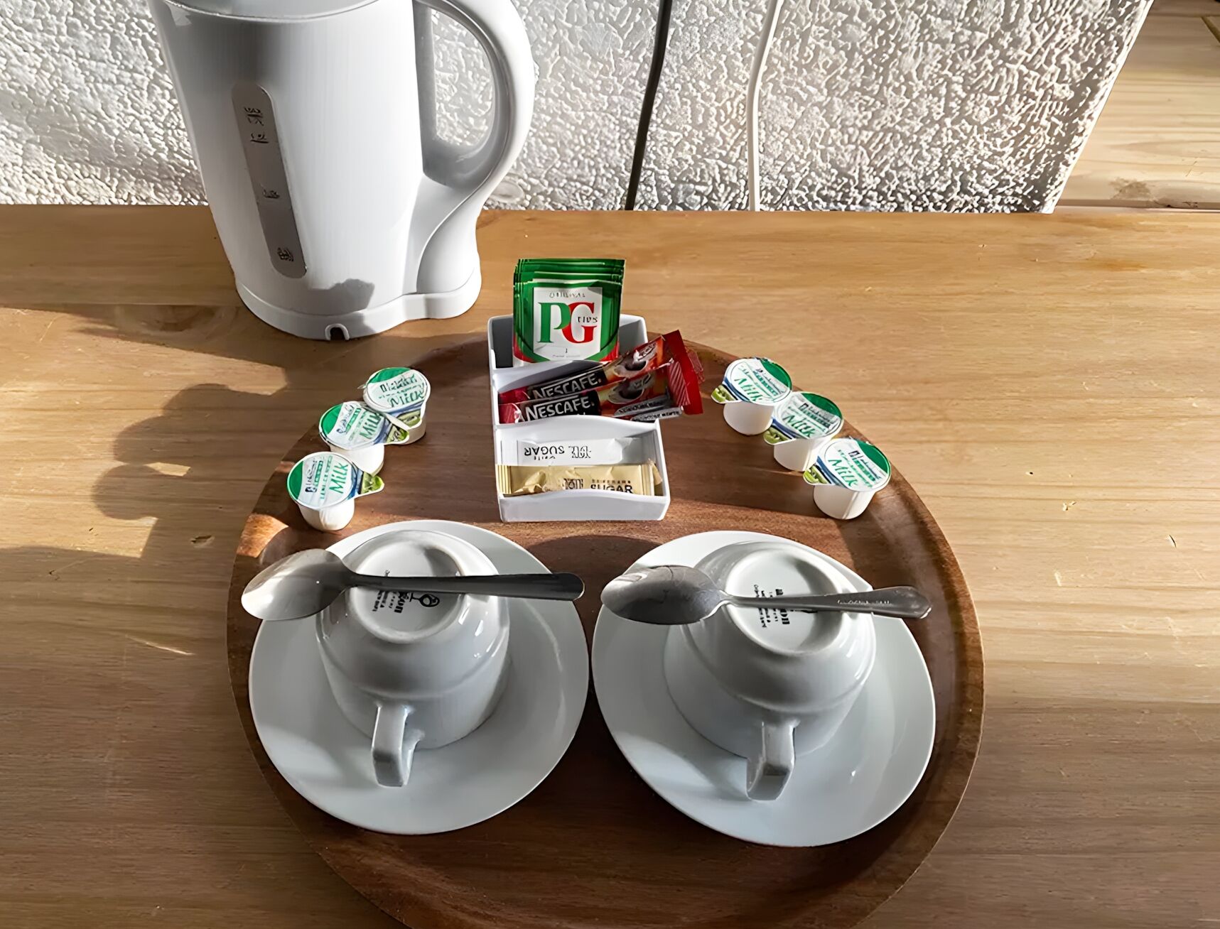 Ein Tablett mit zwei weißen Tassen, einer Packung Nescafe Instantkaffee und mehreren kleinen Milchbehältern auf einem Holztisch.