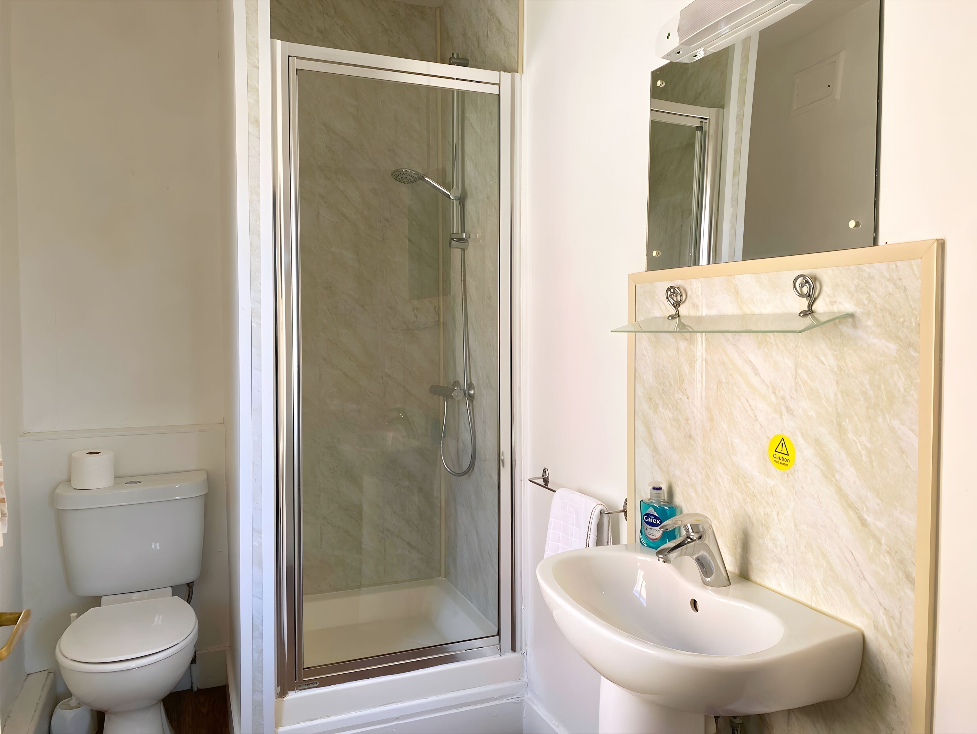 Une salle de bain comprenant des toilettes, une douche fermée par une paroi de verre et un lavabo avec un miroir au-dessus.