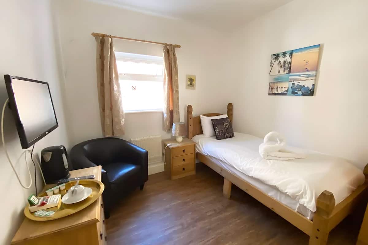 Ein Schlafzimmer mit einem Bett, einem Schreibtisch mit Computer, einem Sessel und einem Fenster mit Vorhängen.