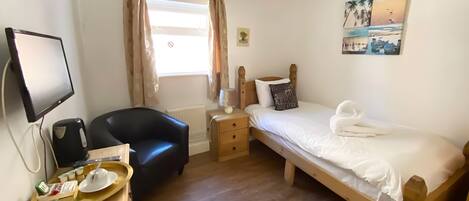 A bedroom with a bed, a desk with a computer, a chair, and a window with curtains.