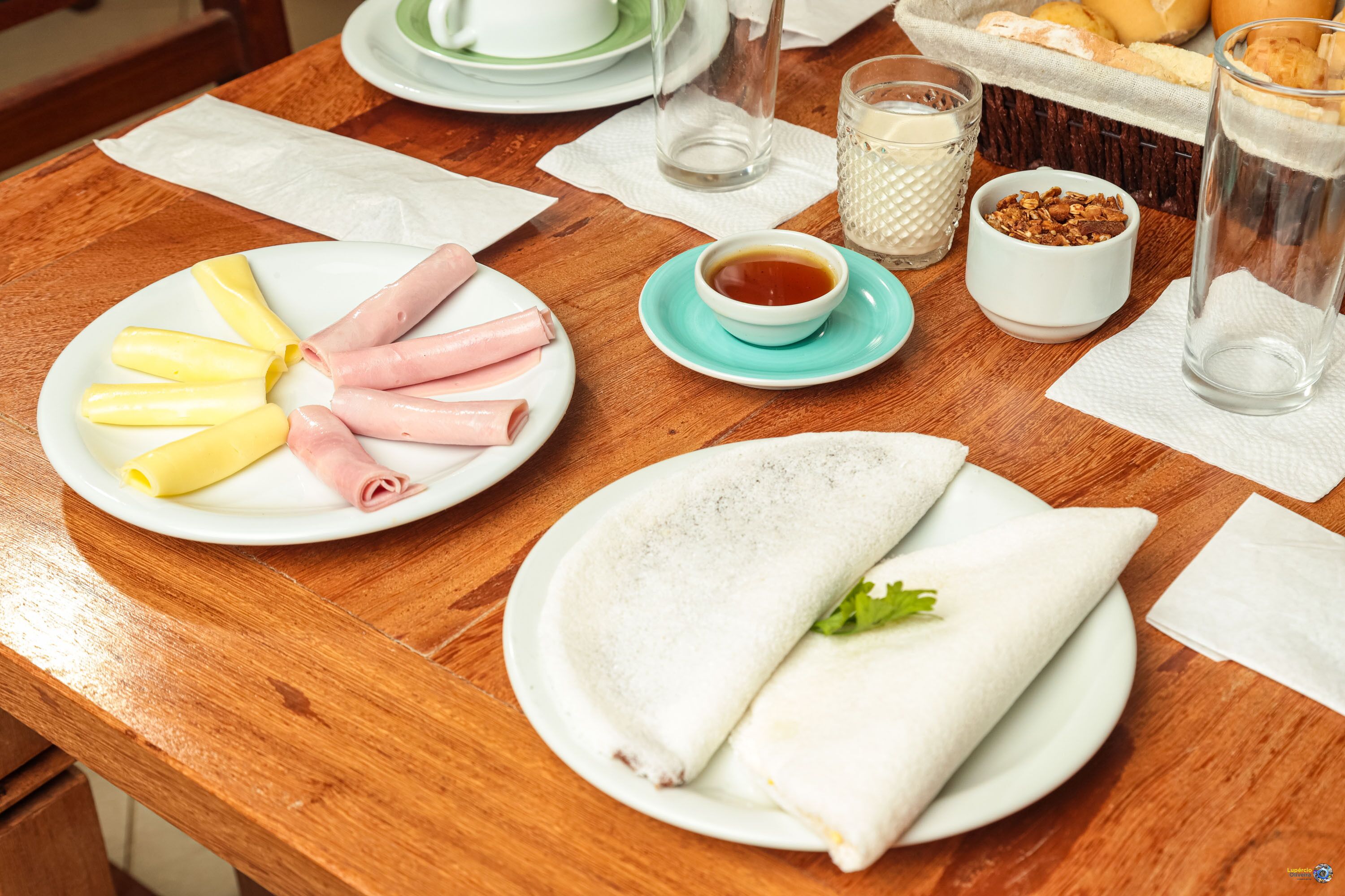 Una mesa de madera con platos de comida, incluyendo un plato de carnes cortadas, un tazón de sopa y una crepe doblada.