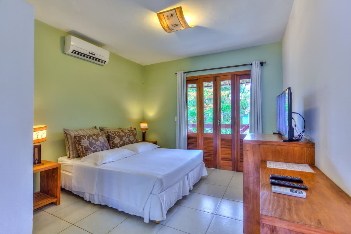 Quarto com cama, luminárias de cabeceira, televisão e ar condicionado.