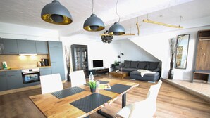 A modern kitchen with grey cabinets, a built-in oven, and a dining area with a wooden table and chairs. - Haus Shiralee (Rostock)