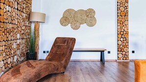 A modern lounge area with a curved lounge chair, a bench, and a wall decorated with stacked logs. - Haus Shiralee (Rostock)