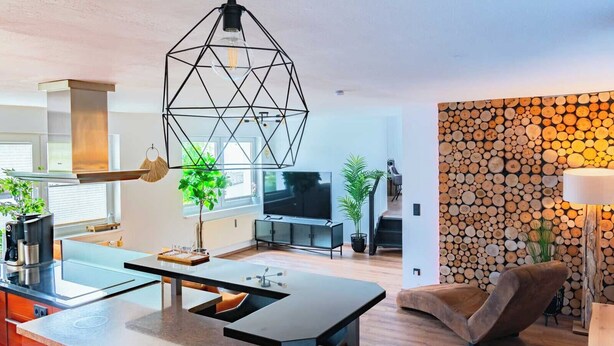 A modern kitchen with a central island, a dining area with a brown leather chair, and a living room with a TV and plants. - Haus Shiralee (Rostock)