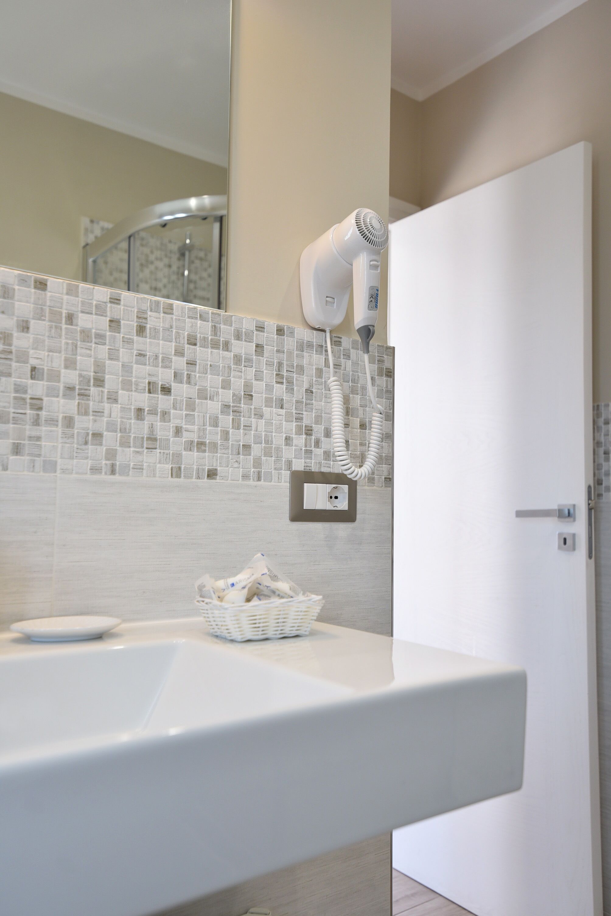 A modern bathroom with a white sink, a hairdryer on the wall, and a tiled backsplash.
