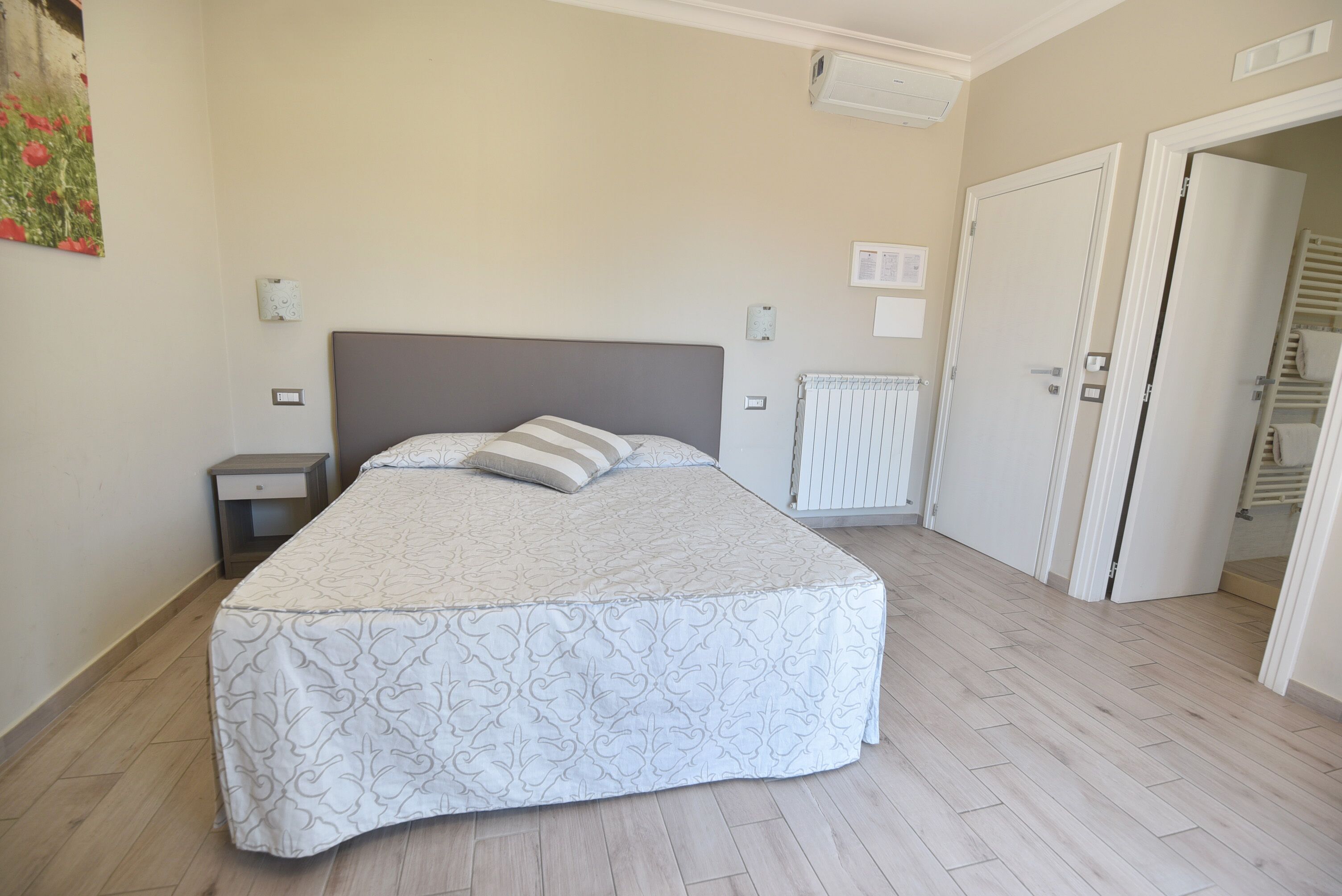 Um quarto com cama, mesas de cabeceira, radiador e guarda-roupa.
