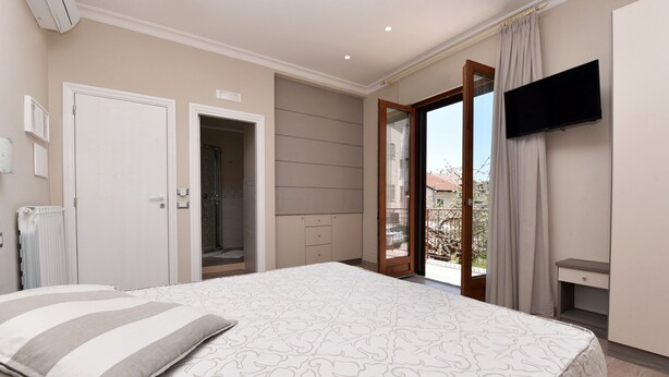 Une chambre à coucher comprenant un lit, une télévision, une salle de bain et donnant sur l’extérieur.