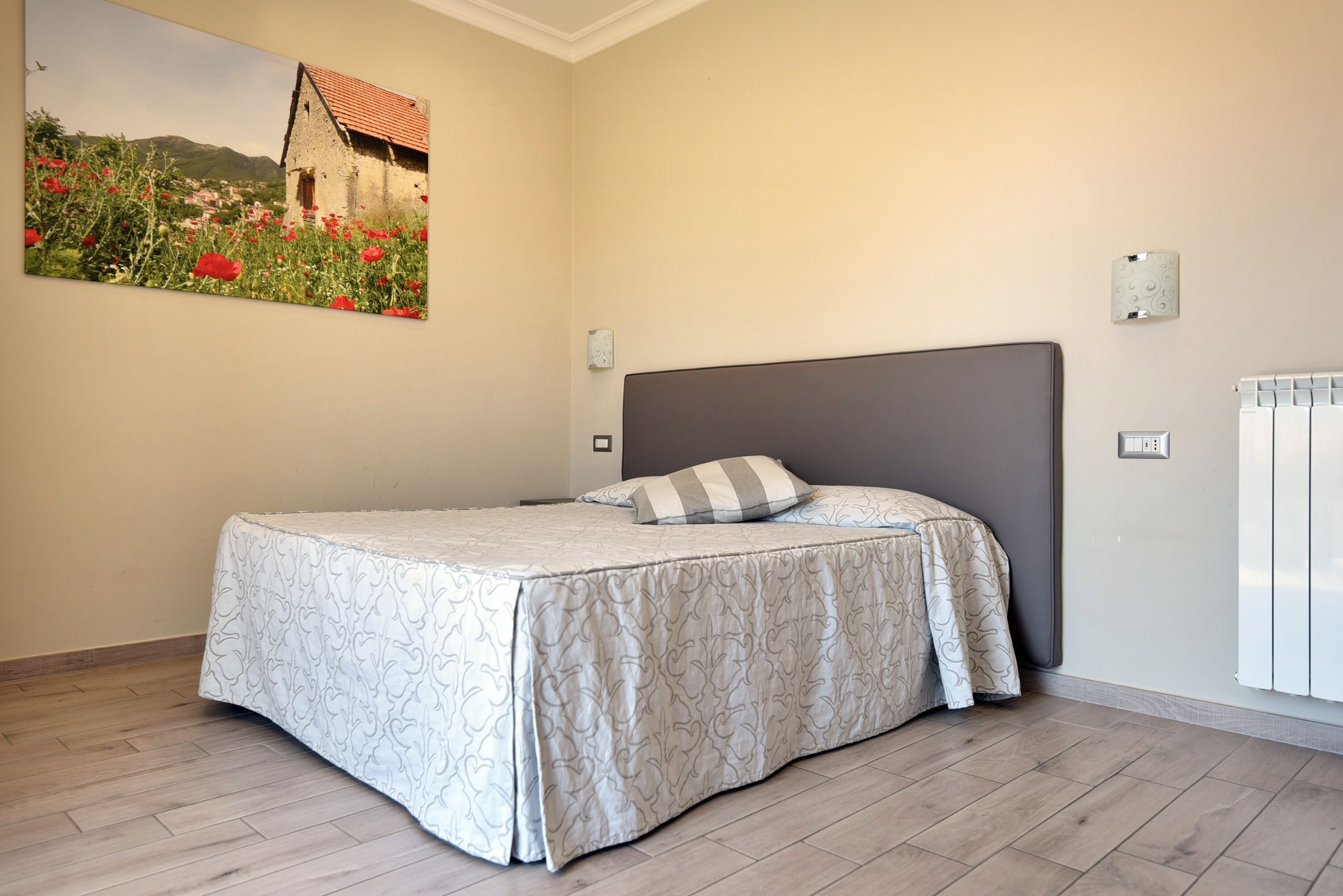 A bedroom with a bed, a headboard, a wall-mounted light, and a radiator.