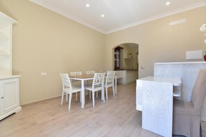 Un coin repas avec une table et des chaises, une cuisine en arrière-plan et un meuble blanc sur la gauche.