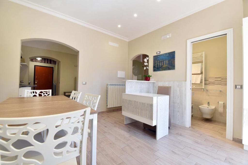 Ein modernes Interieur mit einem Essbereich, einem weißen Empfangstresen und einem durch eine geöffnete Tür einsehbaren Badezimmer.