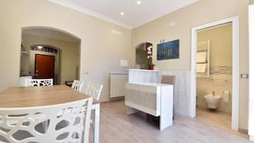 Ein modernes Interieur mit einem Essbereich, einem weißen Empfangstresen und einem durch eine geöffnete Tür einsehbaren Badezimmer.