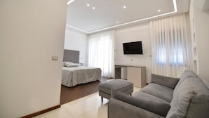 A modern hotel room with a bed, a sofa, a TV, and a desk. - Relais Milò (Agerola)